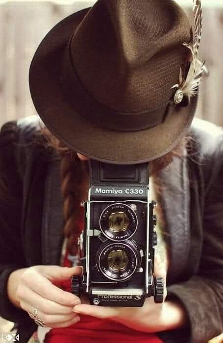 A woman wearing a hat covering her face, holding a phone, taking pictures